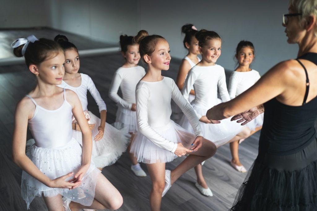 Ballet teacher and students ballerinas exercising in dance class in school